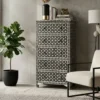 Black bone inlay 5 drawer tall chest of drawers placed in modern living room with white chair and plant