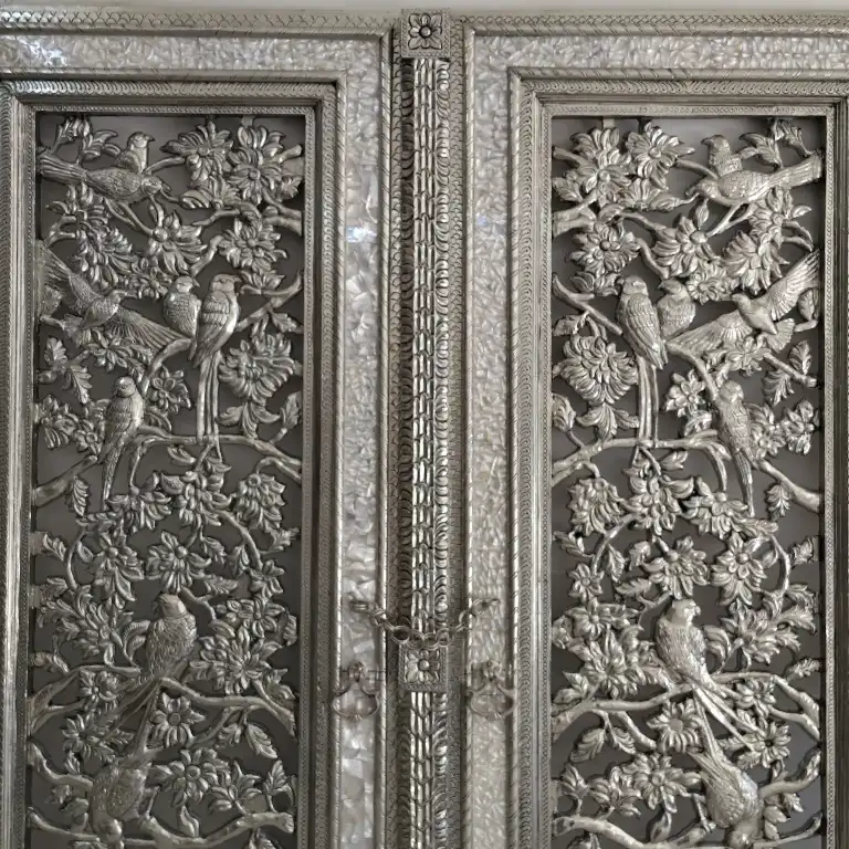 Detailed bird and flower carvings on a decorative silver-toned temple door